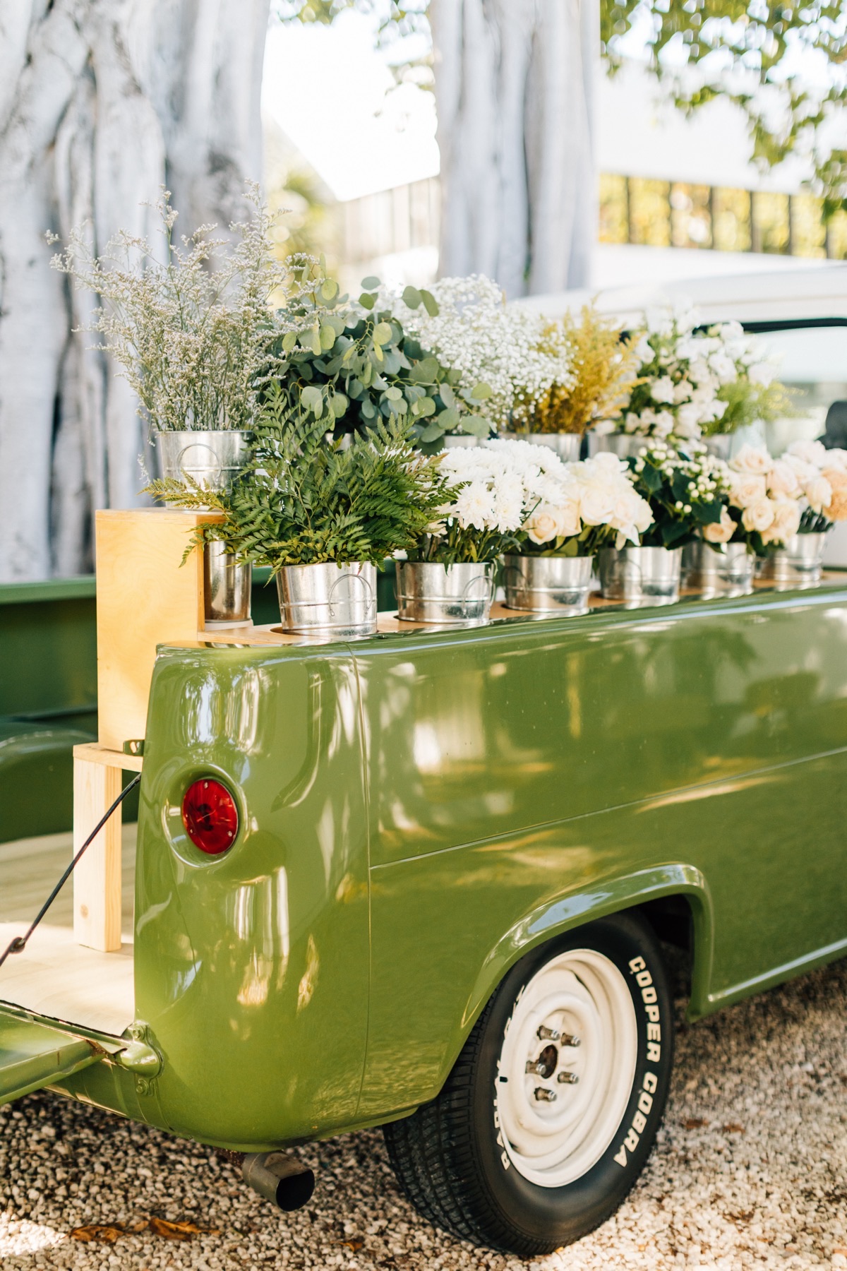 The rear of the green Birdie truck on gravel, its bed lined with silver buckets of white flowers and greenery.