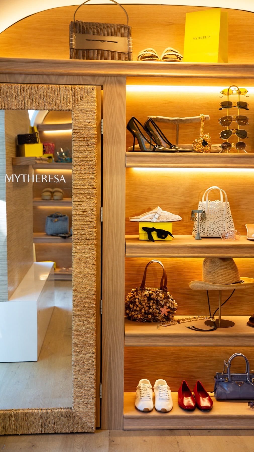 Lit wooden shelving inside the trailer displaying handbags, shoes and accessories beside a full-length mirror.