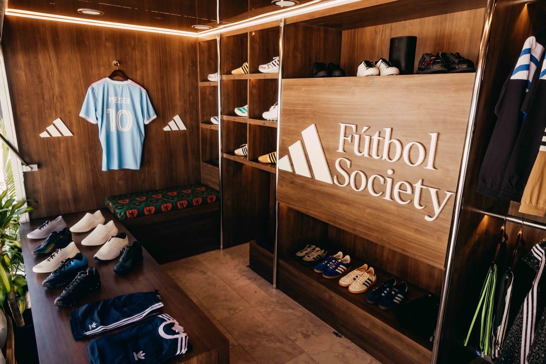 Inside the Adidas truck: wood-paneled walls, a 'Fútbol Society' sign, lit shelves of sneakers and a light-blue number 10 jersey on the wall.