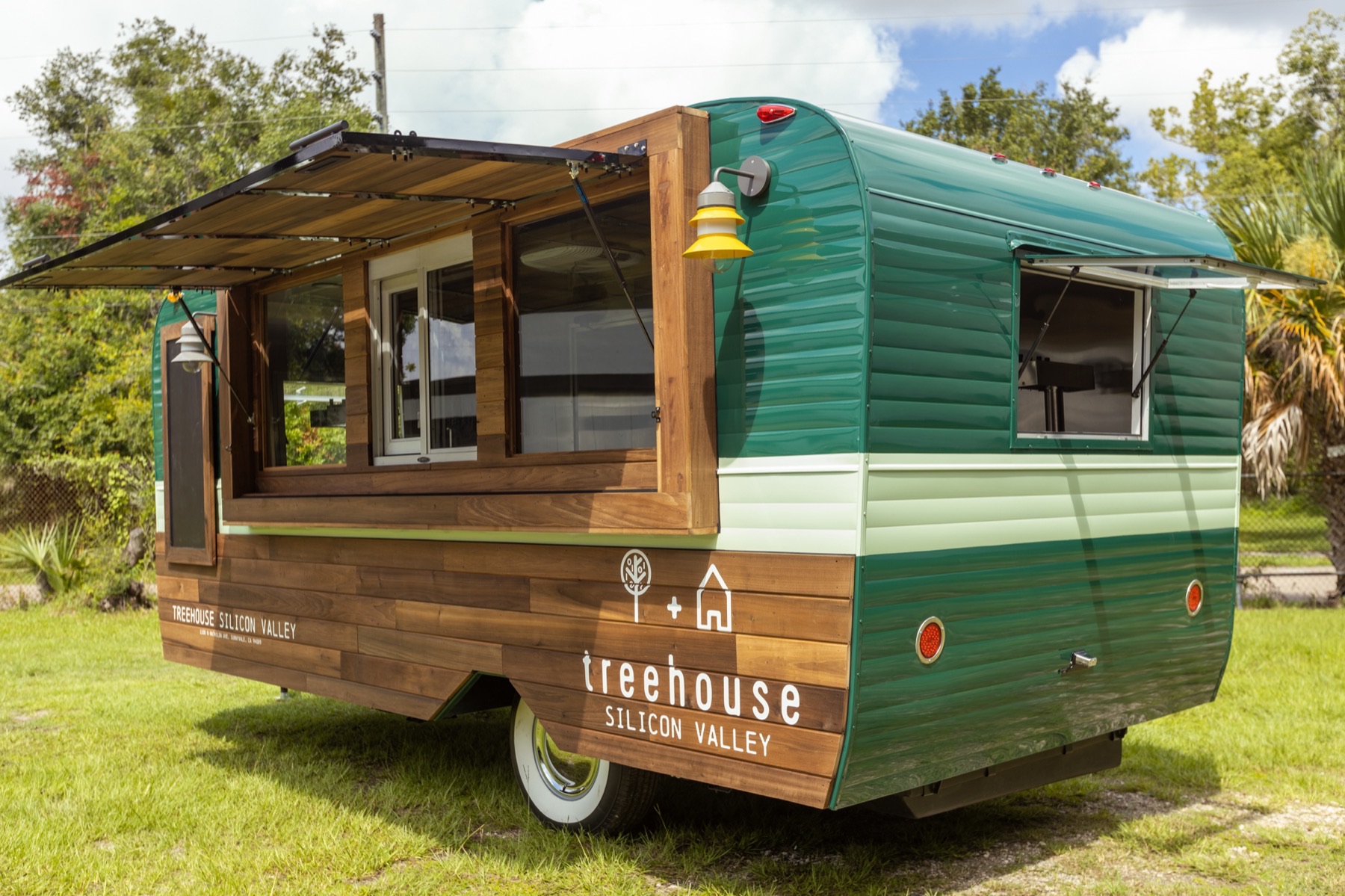 A rounded green trailer with a mint stripe and horizontal timber cladding on its lower half, its long side opened to a wood-framed bar counter under a propped awning, painted with the Treehouse tree-and-house logo and "treehouse Silicon Valley."